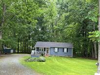 Charming single-story home with blue siding, flower boxes and lush green lawn surrounded by mature trees at 1634 Hurdle Mills Rd, Roxboro, NC 27574