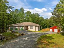 Charming home with a gravel driveway, lush green trees and red barn on a sunny day at 121 Pheasant Ct, Pittsboro, NC 27312