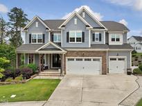 Two-story home featuring gray siding, a stone-accented garage, and a charming covered front porch with stone footers at 213 Lofty Oak Ln, Holly Springs, NC 27540
