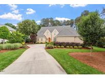 Beautiful brick home with lush green lawn, mature trees and long driveway on a partially cloudy day at 8904 Milden Hall Ct, Raleigh, NC 27615