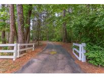 Long, winding driveway through lush woods with white fencing at the entrance at 117 Carolina Forest Rd, Chapel Hill, NC 27516