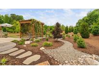 Beautiful backyard with stone walkway, mulch, and wooden pergola covered in climbing vines and surrounding greenery at 829 Churton Pl, Cary, NC 27518