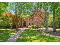 Two story brick home with black front door surrounded by mature trees and a green lawn at 7309 New Forest Ln, Wake Forest, NC 27587