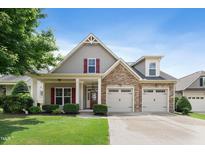 Charming home showcasing manicured lawn, stone accents, a two-car garage, and red shutter details against a blue sky at 13 Nettletree Creek Ct, Youngsville, NC 27596