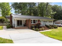 Charming one story home with a metal roof, brick and gray siding and mature landscaping at 203 W Boundary St, Cary, NC 27513