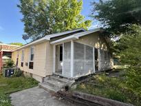 Front exterior view of a single-story home with light-yellow siding, overgrown landscaping and a concrete driveway at 2302 Chautauqua Ave, Durham, NC 27707