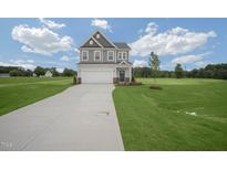 Two-story home featuring a concrete driveway, gray siding, and a well-manicured lawn with an open field in the background at 91 Merle Way Way, Wendell, NC 27591