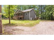 View of the side and rear of the house showing the wooden porch, gravel driveway, and lush trees at 1027 Holden Rd, Youngsville, NC 27596