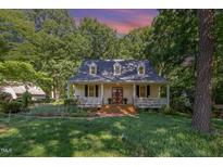 Charming home with a welcoming front porch, brick walkway, and surrounded by lush greenery and trees at 9417 Greenfield Dr, Raleigh, NC 27615
