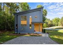 Modern exterior with gray siding, wood accents, and gravel driveway, nestled in a lush, green setting at 160 Daphine Dr, Hillsborough, NC 27278