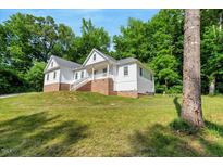 Charming two-story home with white siding, brick foundation, and a lush green lawn surrounded by trees at 10304 Stallion Way, Bahama, NC 27503
