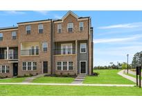 Beautiful brick townhouse featuring a small balcony, green lawn and gray siding under a blue sky at 209 Broomgrove Way, Wake Forest, NC 27587