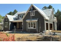 New construction home featuring gray vertical siding, white trim, and ladders for painting, with a builder on the ladder at 93 Bur Oak Ct, Pittsboro, NC 27312