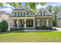 Charming brick home featuring a covered front porch, manicured lawn, and mature landscaping at 117 Synandra Ln, Holly Springs, NC 27540