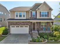 Charming two-story home featuring a stone facade, covered porch, attached two-car garage, and manicured landscaping at 241 Fishburn Dr, Apex, NC 27523