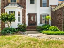 Inviting brick and white facade with a stylish wood door, complemented by lush landscaping and manicured lawn at 5708 Big Sandy Dr, Raleigh, NC 27616