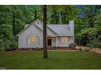 Charming home boasts lush green lawn, white siding, brick foundation, mature trees, and professionally landscaped front yard at 702 Sanderson Dr, Durham, NC 27704