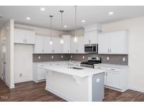 Modern white kitchen featuring an island, stainless steel appliances, and stylish backsplash at 3920 Well Fleet Dr, Fuquay Varina, NC 27526