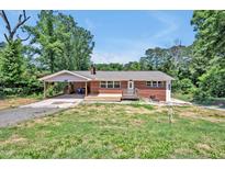 Charming brick home featuring a carport and a wooden porch, surrounded by a partially wooded lot at 112 S Joyland St, Durham, NC 27703
