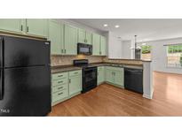 Well-lit kitchen showcasing sage green cabinets, a mosaic backsplash, black appliances, and hardwood floors at 1120 Renewal Pl # 111, Raleigh, NC 27603