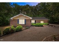 Charming brick ranch home featuring manicured landscaping and a spacious gravel driveway surrounded by mature trees at 1134 Deerfoot Trail Trl, Sanford, NC 27332