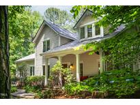 Charming home exterior with classic architectural details, covered porch, and lush landscaping in a wooded setting at 574 Chatham Dr, Chapel Hill, NC 27516