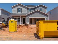 Unfinished two-story home featuring gray siding and an open garage with construction equipment and a portable toilet at 744 Deschutes Dr, Garner, NC 27529