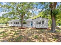Charming white brick home with a metal roof, blue front door, and mature trees shading the manicured front yard at 2003 Broadway Rd, Sanford, NC 27332