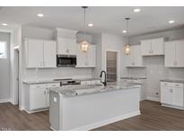 New kitchen features white cabinets, granite countertops, stainless appliances and modern pendant lighting at 224 Wild Turkey Way, Lillington, NC 27546