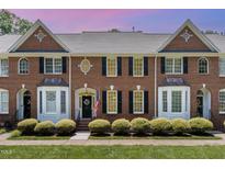 Charming brick townhome featuring a black front door and lush landscaping, complemented by a manicured lawn at 227 Kenmont Dr, Holly Springs, NC 27540