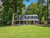 Charming two-story home boasts a welcoming front porch and a lush, green lawn surrounded by mature trees at 1215 Brookgreen Dr, Cary, NC 27511