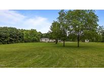 View of the property's green front yard with large trees and a house in the background on a sunny day at 5200 Mrs Fuller Rd, Mebane, NC 27302