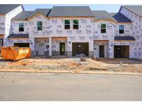 Exterior view of a townhome construction site showing Tyvek HomeWrap, garage doors, and building materials at 1033 Winding Spring Dr, Mebane, NC 27302