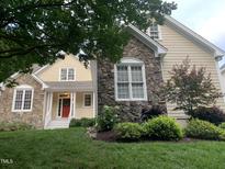 Charming home showcasing stone accents, neutral siding, a red front door with a wreath, and manicured landscaping at 1012 Coram Fields Rd, Wake Forest, NC 27587