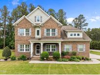 Beautiful two-story brick home with a manicured lawn, complemented by lush landscaping and gray shutters at 21 Botanical Way, Pittsboro, NC 27312
