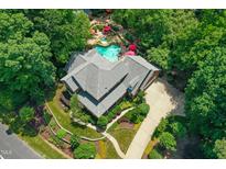 Aerial view of a luxury house with a uniquely shaped pool, red umbrellas, mature trees, and a winding driveway at 4021 Chaumont Dr, Apex, NC 27539