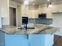 Modern kitchen featuring stainless steel appliances, granite counters, light backsplash, and white cabinetry at 204 Seahawk Way, Zebulon, NC 27597
