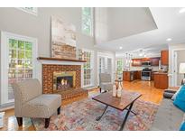 Cozy living room featuring a brick fireplace, hardwood floors, and a view into the adjacent kitchen at 106 Ridgepath Way, Cary, NC 27511