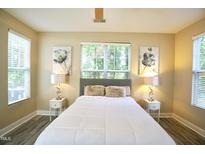 Bright bedroom features wood flooring, a comfortable bed, side tables, and large windows for natural light at 1912 Parkside Village Dr, Clayton, NC 27520