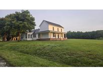 Two-story farmhouse featuring a covered porch, expansive yard, and lush green landscape at 8365 Aaron Creek Church Rd, Oxford, NC 27565