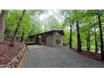 Stunning exterior elevation of modern home featuring walls of glass, brick entryway, and gravel driveway surrounded by lush forest at 1 Davie Ln, Chapel Hill, NC 27514