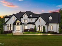 A grand two-story home featuring a manicured lawn, striking white brick, and black trim against a colorful sunset sky at 2220 Inwood Landing Ct, Raleigh, NC 27603