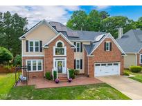 Charming brick and siding home featuring a two-car garage, solar panels, and landscaped front yard with a pergola swing at 8913 Walking Stick Trl, Raleigh, NC 27615