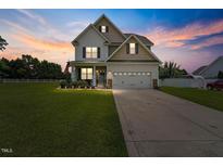 Inviting two-story home featuring a manicured lawn and a charming two-car garage, displayed under a captivating twilight sky at 15 Scuppernong Ln, Lillington, NC 27546