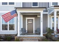 Charming front porch with gray chairs and an American flag, leading to a stylish gray front door at 728 Silo Park Dr, Wake Forest, NC 27587