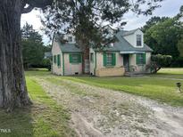 Charming cottage-style home with a stone facade, green shutters, and a gravel driveway, nestled amidst mature trees at 45 Perkinson St, Kittrell, NC 27544