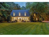 Charming two-story home with a lush green lawn, manicured landscaping, and mature trees at dusk at 5344 Mill Dam Rd, Wake Forest, NC 27587
