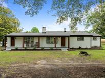 Charming white brick home boasts a covered porch with wooden columns, inviting rocking chairs, and beautifully landscaped front yard at 7042 Us 401 Highway N, Fuquay Varina, NC 27526