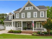 Traditional two-story home with a covered front porch, American flag, green siding, and manicured lawn at 821 Rambling Oaks Ln, Holly Springs, NC 27540