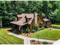 Charming log home with stone chimney, landscaped yard, and inviting front porch with the American flag at 2416 Kearney Rd, Wake Forest, NC 27587